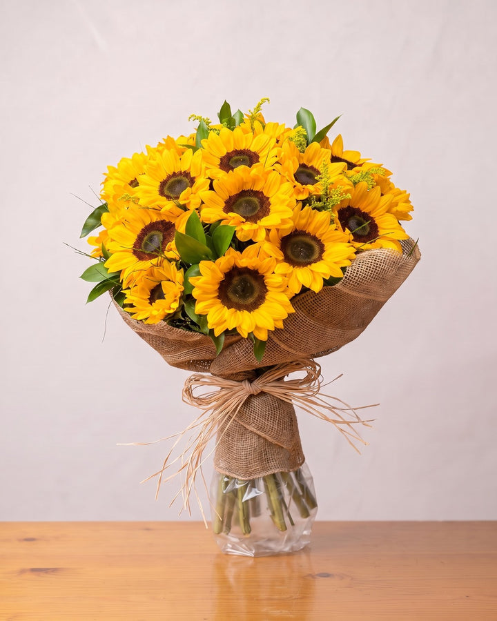 Buquê de 20 girassóis: girassóis com solidago numa gola de juta amarrada com ráfia, segurado por uma mão