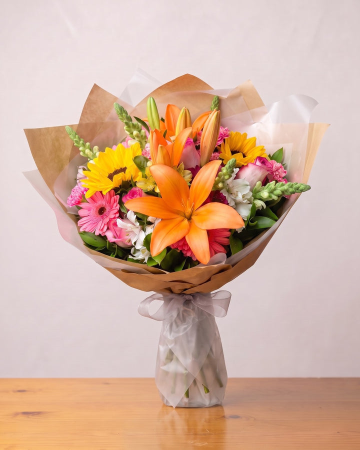 Buquê mix clássico: lírio laranja, dois girassóis, gérberas, cravos e rosas cor-de-rosa em papel kraft