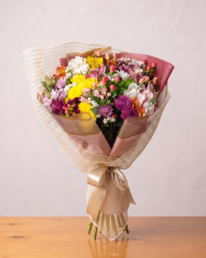 Buquê mix de flores do campo: crisântemos amarelos e roxos, alstroemérias e hypericum em papel rosado e tela creme